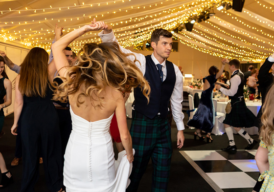 Bride and groom dancing under draped fairy light ceiling